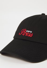 Boné preto feito de algodão, com texto bordado vermelho e branco "zero Stress". Visor curvado com detalhes em tecido texturizado.