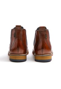 Bottes chevilles en cuir marron avec des panneaux élastiques sur les côtés et des coutures contrastées ; la semelle en caoutchouc présente un accent bleu subtil près du talon.