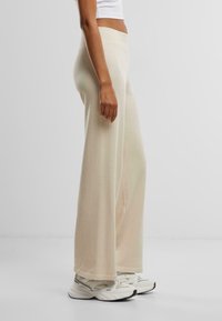 Pantaloni beige a gamba larga realizzati in tessuto morbido con vita alta, caratterizzati da una texture liscia e un design lungo fino al pavimento.
