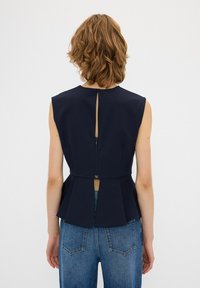 Top peplum blu navy con spalle strutturate, apertura a chiave sul retro e dettaglio con zip. Realizzato in un tessuto liscio e rigido. Abbinate a jeans blu.