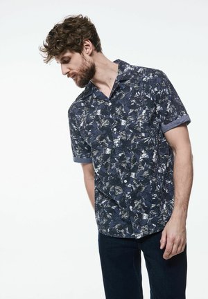 Camisa de botones de manga corta con un patrón abstracto en azul marino, con cuello extendido y puños en azul claro. Confeccionada en tela ligera.