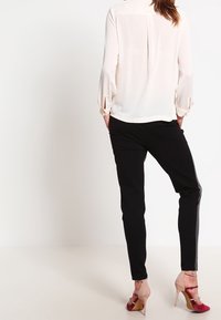 Blusa cremosa a maniche lunghe con polsini arricciati abbinata a pantaloni neri aderenti; tacchi a strappo rossi e rosa accentuano l'outfit.