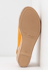 Semelle d’une sandale compensée jaune avec un talon en liège, taille 4½, montrant une semelle extérieure en caoutchouc beige lisse et le nom de la marque "butterfly."