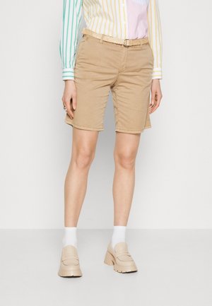 Beige bermudashorts lavet af bomuld, med flettet bælte, sidelommer og lige pasform, kombineret med træsko og hvide sokker.