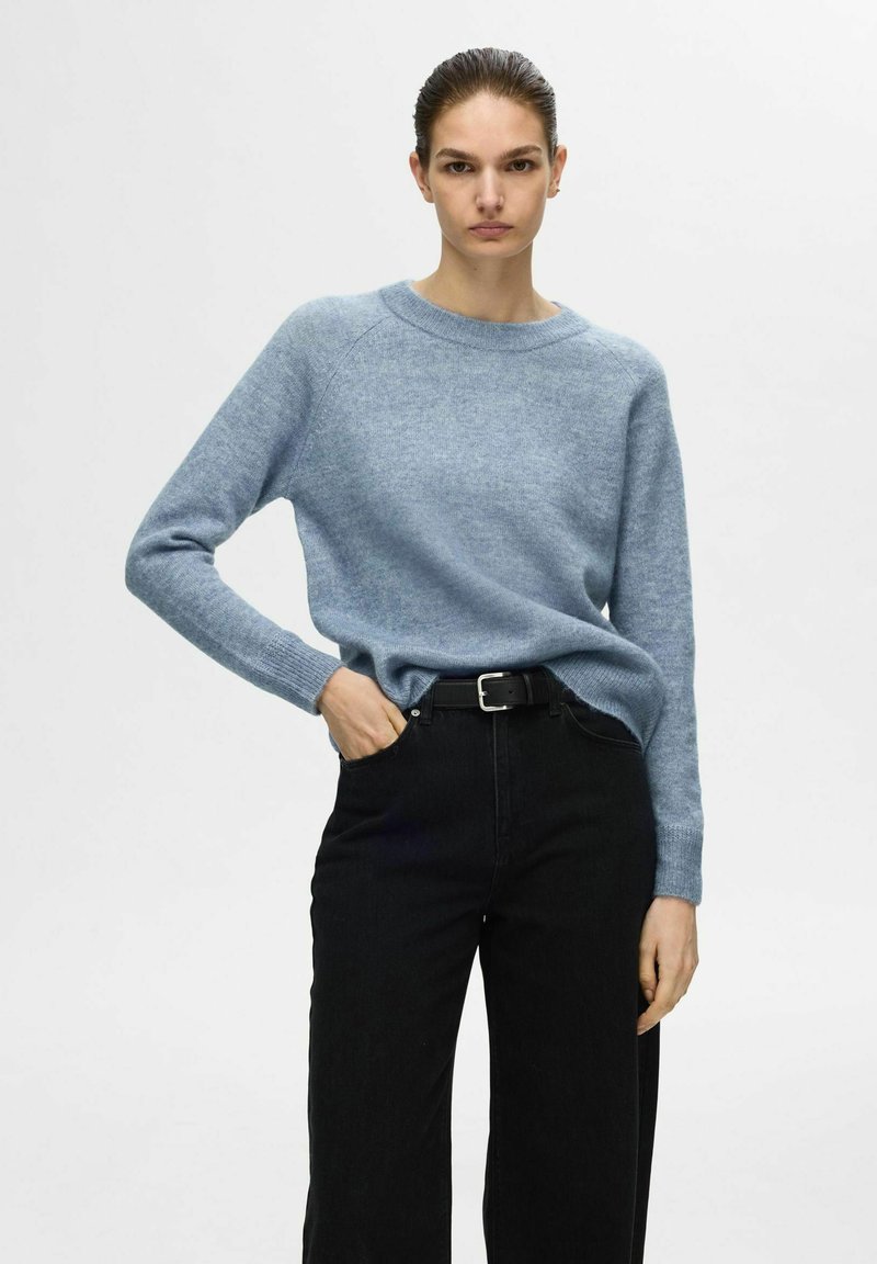Lichtblauwe trui met een ronde hals en lange mouwen, gecombineerd met zwarte wijdvallende jeans. De stof lijkt zacht en lichtjes textuur te hebben.