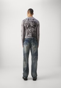 Gray long-sleeve shirt with abstract black print, paired with loose-fitting blue jeans featuring faded areas and stitched back pockets.