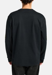 Black long-sleeve shirt made of cotton, featuring a round neck and printed accents on the sleeves. The fit is relaxed with a straight hem.