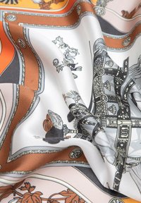 Satin scarf featuring orange, white, and brown colors with intricate patterns depicting flora and decorative hardware accents. Soft texture.