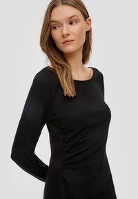 Schwarzes langärmeliges Kleid mit rundem Ausschnitt, glattem Stoff, leichter Raffung an den Seiten, taillierter Silhouette, minimalistisches Design.