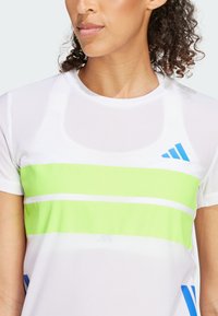 Biely športový tričko so zelenými a modrými horizontálnymi pruhmi, vyrobené z textúrovaného, priedušného materiálu. Obsahuje logo Adidas.