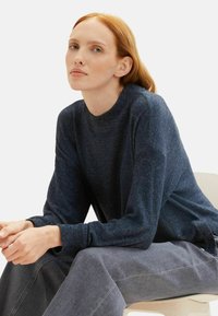Pulover tricotat bleumarin cu guler rotund și mâneci lungi, asortat cu pantaloni gri lejeri. Textură moale cu manșete și tiv din material cu nervuri.