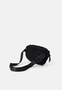 Svart fleece-väska med rundad form, justerbar svart rem och dragkedja. Har en texturerad tygkvalitet för ökad visuell intresse.