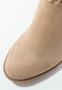 Bout de chaussure en daim beige avec coutures visibles le long du bord de la semelle, mettant en valeur une texture lisse et un design arrondi.