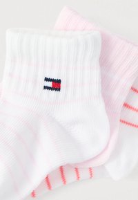 Τρία ζευγάρια διπλωμένες παιδικές κάλτσες σε λευκό και ανοιχτό ροζ με λεπτές ρίγες, μία λευκή κάλτσα έχει μικρό κόκκινο, λευκό και μπλε λογότυπο.
