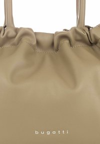 Borsa a tracolla in pelle beige con design a cima arricciata, texture liscia e un logo sottile stampato in bianco alla base.