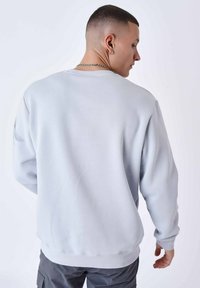 Lichtgrijze sweatshirt met lange mouwen, ribgebreide manchetten en onderrand, met een eenvoudig ontwerp en zachte textuur, gedragen over cargo broeken.