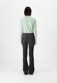 Pull en tricot vert menthe à la coupe décontractée, associé à un jean bootcut foncé. Texture douce et détails côtelés sur le pull.