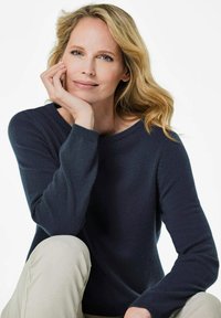 Marineblaues Strickpullover mit Rundhalsausschnitt und langen Ärmeln. Aus weichem, strukturiertem Material gefertigt. Kombiniert mit hellen Hosen.