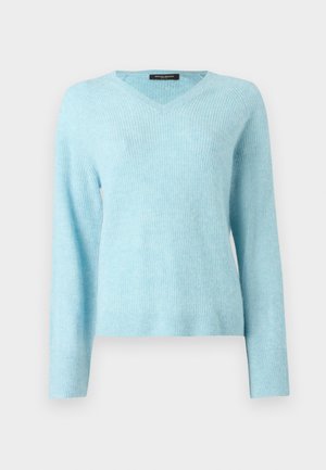 Pull col en V bleu clair, texture douce, associé à une jupe crayon en cuir noir avec une fente latérale, et des chaussures à talons hauts noires.