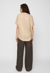 Beige Hemd mit kurzen Ärmeln, vertikalen weißen Streifen, abgerundetem Saum und einer weichen Textur, kombiniert mit dunkelbraunen weit geschnittenen Hosen.