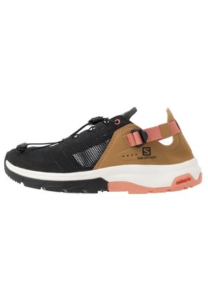 Chaussure de sport noire et brune avec des panneaux en mesh, lacets ajustables, accents roses et une semelle extérieure blanche-orange. Conception légère pour une utilisation en extérieur.
