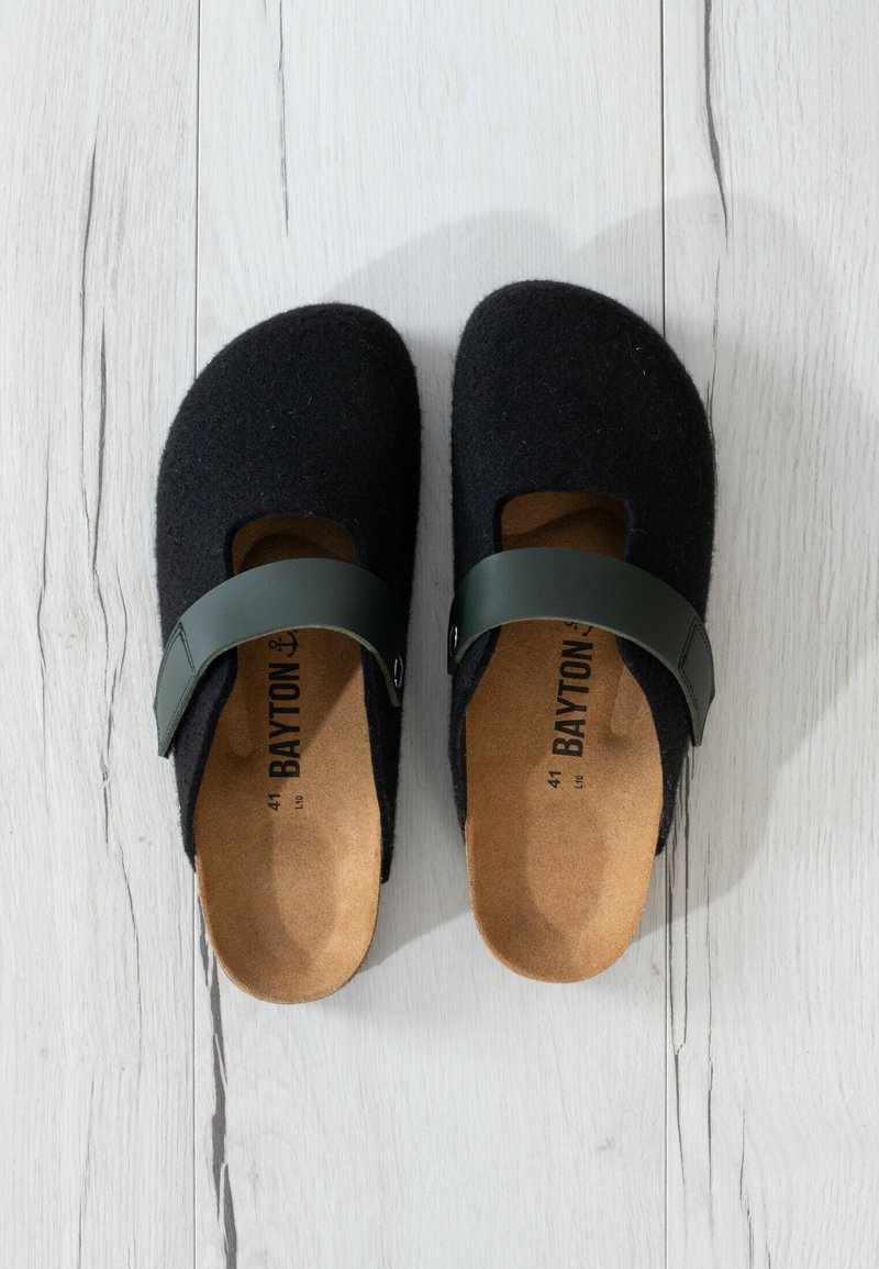 Zuecos de fieltro negro con una correa de cuero verde, punta redondeada y plantilla de corcho natural. Presentan un diseño de corte abierto. Talla 41 impresa en el interior.