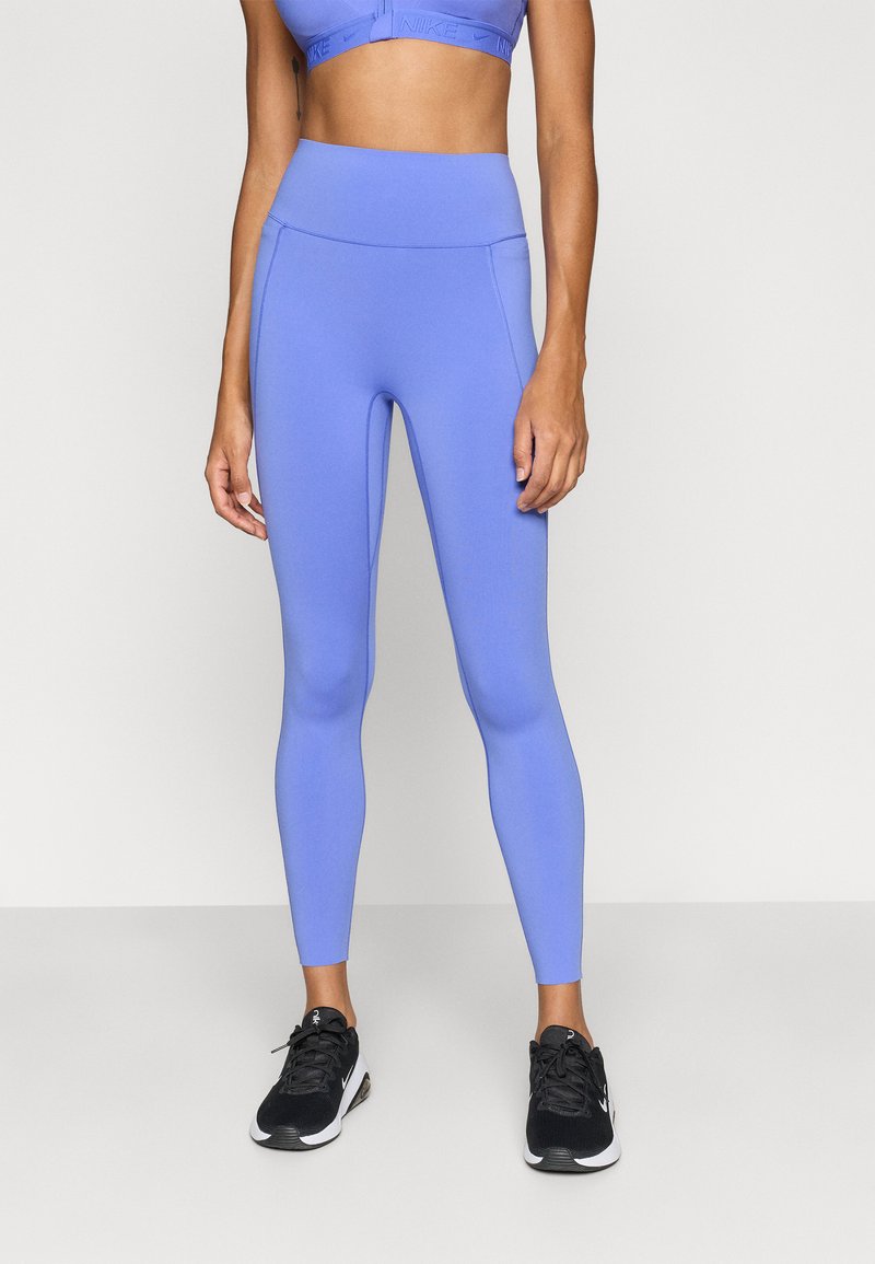 Ανοιχτό μωβ κολάν με ψηλή μέση, κατασκευασμένο από ελαστικό υλικό, σε συνδυασμό με μαύρα αθλητικά παπούτσια με άσπρες λεπτομέρειες.