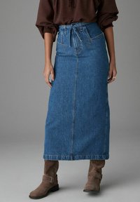 Denim maxi seelik, keskmise pesu, kõrge vöökoht ja sidumisrihm, külgmised õmblustaskud ja sirge siluett. Kombineeritud pruunide pahkluu saapadega.