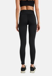 Zwarte hoge taille legging met textuurstof, een ritszak aan de achterkant en een slimfit ontwerp. Gecombineerd met zwarte sportschoenen.