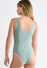 Costume intero color verde chiaro con un motivo testurizzato. Presenta un design con schiena bassa e spalline larghe per una vestibilità comoda.