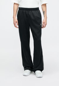 Čierne športové nohavice s elastickým pásom, bočnými pruhmi a malým logom na ľavej strane. Vyrobené z hladkej, ľahkej látky.