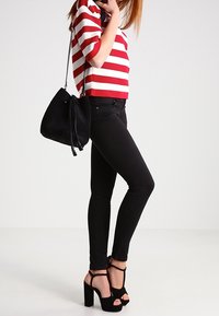 Gestreiftes Kurzarm-Shirt in Rot und Weiß, schwarze Skinny-Jeans, schwarze Bucket-Bag und schwarze hochhackige Sandalen mit Knöchelriemen.