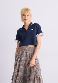 Navy cropped polo with a V-neck and white stripes on the collar and sleeves. Paired with a tiered plaid skirt in muted colors.