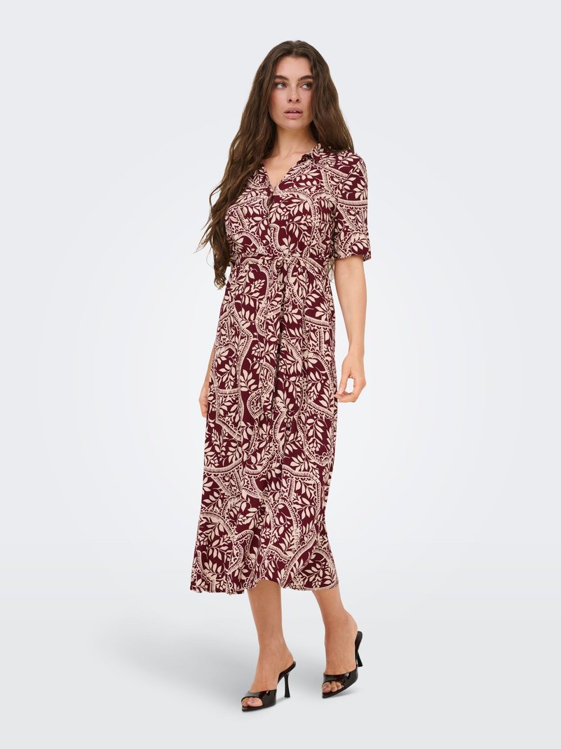 Femme portant une robe midi bordeaux avec des motifs floraux beiges, manches mi-longues et taille nouée, assortie à des talons noirs à bout ouvert.