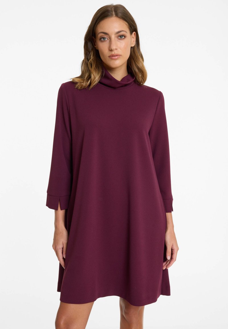 Robe bordeaux à coupe décontractée, col drapé, manches trois-quarts et fentes discrètes sur les manches. Confectionnée dans un tissu lisse et doux.