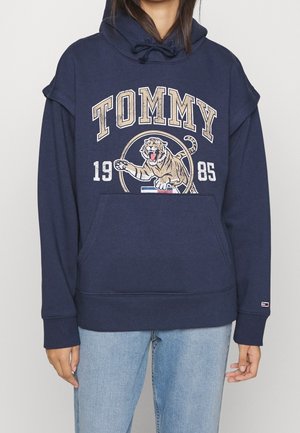 Sudadera azul marino con un gran gráfico de tigre, texto "TOMMY", bolsillo tipo canguro y capucha con cordón. Fabricada con una suave mezcla de algodón.