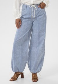 Široké kalhoty vyrobené z lehkého materiálu, s modro-bílými vertikálními pruhy, elastickým pasem s tkaničkou a nařaseným kotníkem.