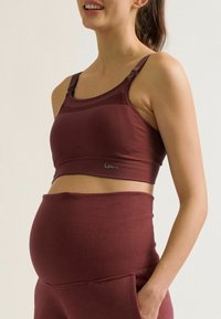 Soutien-gorge de maternité bordeaux avec des bretelles réglables, un tissu texturé et un détail logo. Associé à un pantalon taille haute assorti.