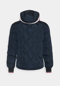 Mörkblå quiltad pufferjacka med diamantstickning, ribbade muddar i röd och vit, och en huva med vit och röd foder.