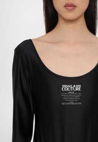 Camiseta negra de manga larga hecha de una tela suave, con un escote redondeado y un logotipo impreso en blanco en el centro.