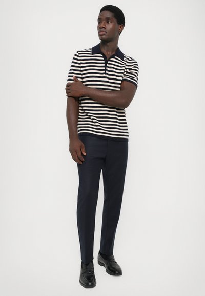 Camiseta tipo polo a rayas en azul marino y crema con cuello, combinada con pantalones azul marino y mocasines negros. Textura de punto suave, manga corta.