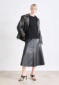 Melnas ādas motociklistu jaka pāri melnam topam, apvienota ar melnu ādas midi svārku un melnā un brūnā krāsā zābakiem uz augstiem papēžiem, visi ar strukturētām dizaina līnijām.