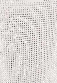 Tessuto bianco scintillante ricoperto da numerosi piccoli strass argentati rotondi disposti in un motivo a griglia con una texture liscia.