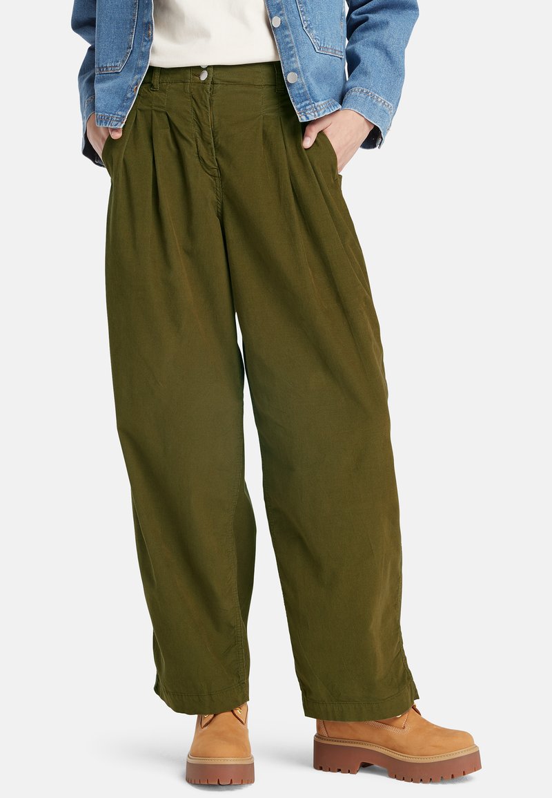 Grüne weite Hose mit Falten, aus Baumwollstoff, mit hoher Taille. Kombiniert mit braunen Schnürstiefeln, was ein lässiges Outfit ergibt.