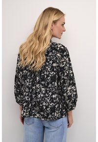 Sort og hvid blomsterbluse med lange ærmer, løs pasform, tekstureret stof og samlede detaljer bagpå, parret med lyseblå jeans.