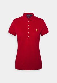 Camisa polo roja de algodón con cuello, mangas cortas, cinco botones y un pequeño logo amarillo en el lado izquierdo del pecho. Textura suave.