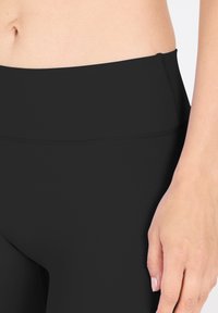 Leggings noirs taille haute en matériau lisse et extensible. Dotés d'une taille plate et d'un design ajusté. Aucun motif ou accent visible.