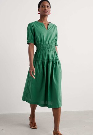 Grünes Kurzarmkleid mit V-Ausschnitt, gerafftem Bund und gestuftem Rock. Hergestellt aus leichtem Stoff mit glatter текстура.