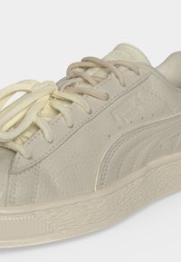 Κοντινό πλάνο ενός ανοιχτό μπεζ sneaker Puma Suede Classic που δείχνει υφασμένο δέρμα, κορδόνια και ανάγλυφο λογότυπο της μάρκας στο πλάι.