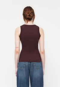 Débardeur côtelé bourgogne avec une coupe ajustée et un col rond, associé à un jean en denim bleu ample, mettant en avant un style décontracté.